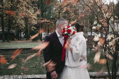 Newlywed couple kissing among falling leaves in a scenic autumn park.